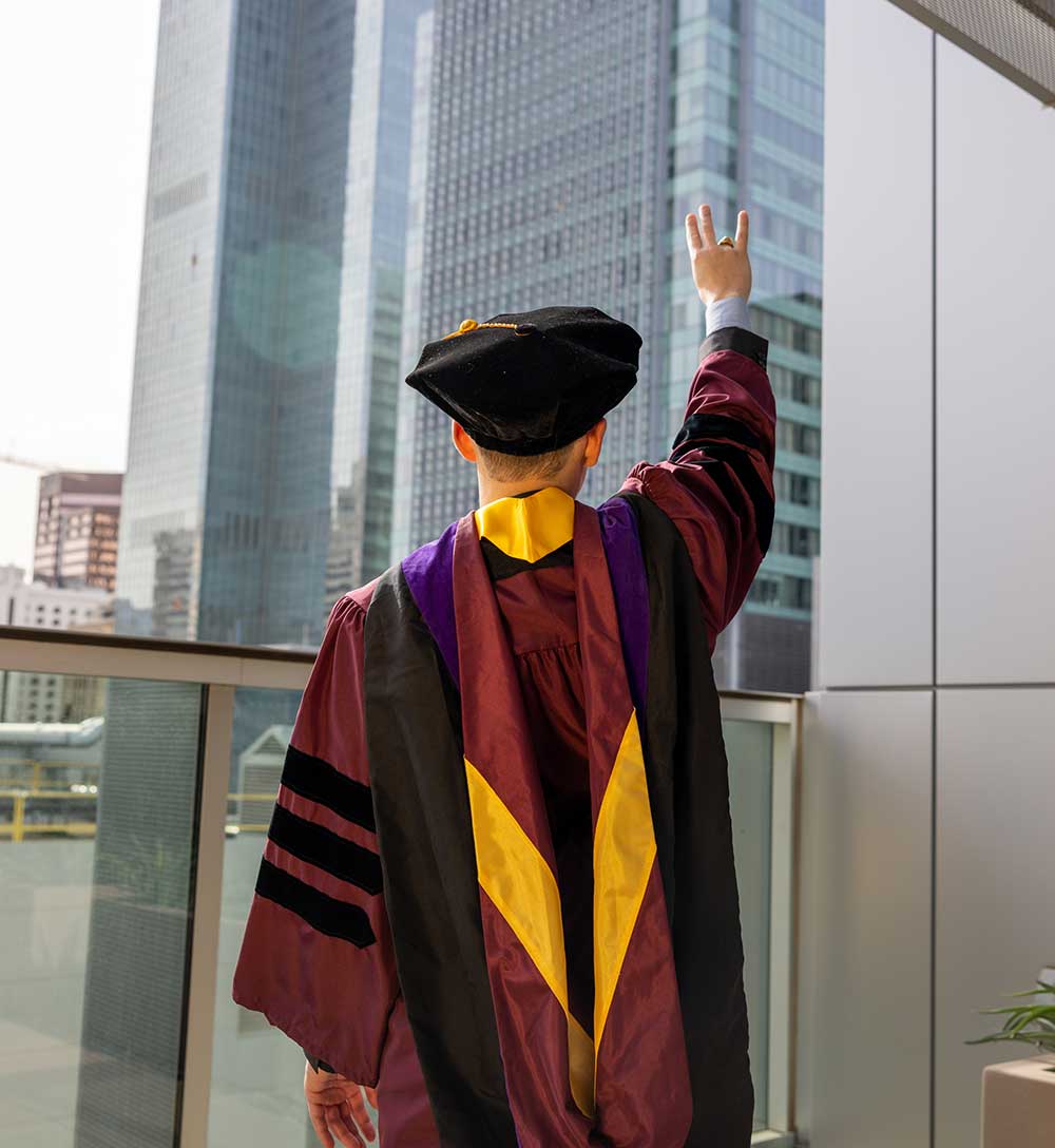 Man in graduation cap and gown holding up hand making the fork symbol